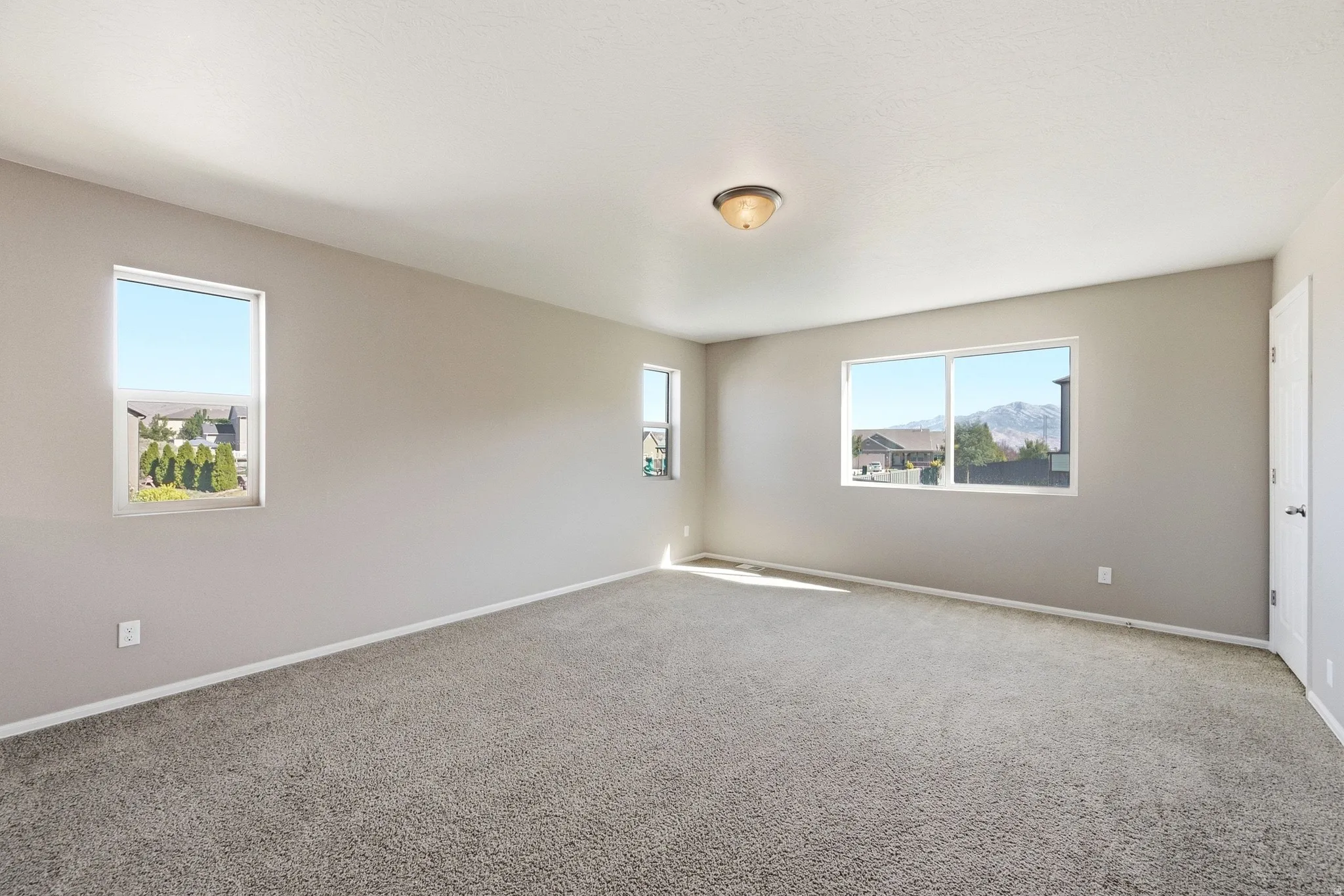 Spacious room featuring neutral carpeting, multiple windows, and a flush mount ceiling light fixture
