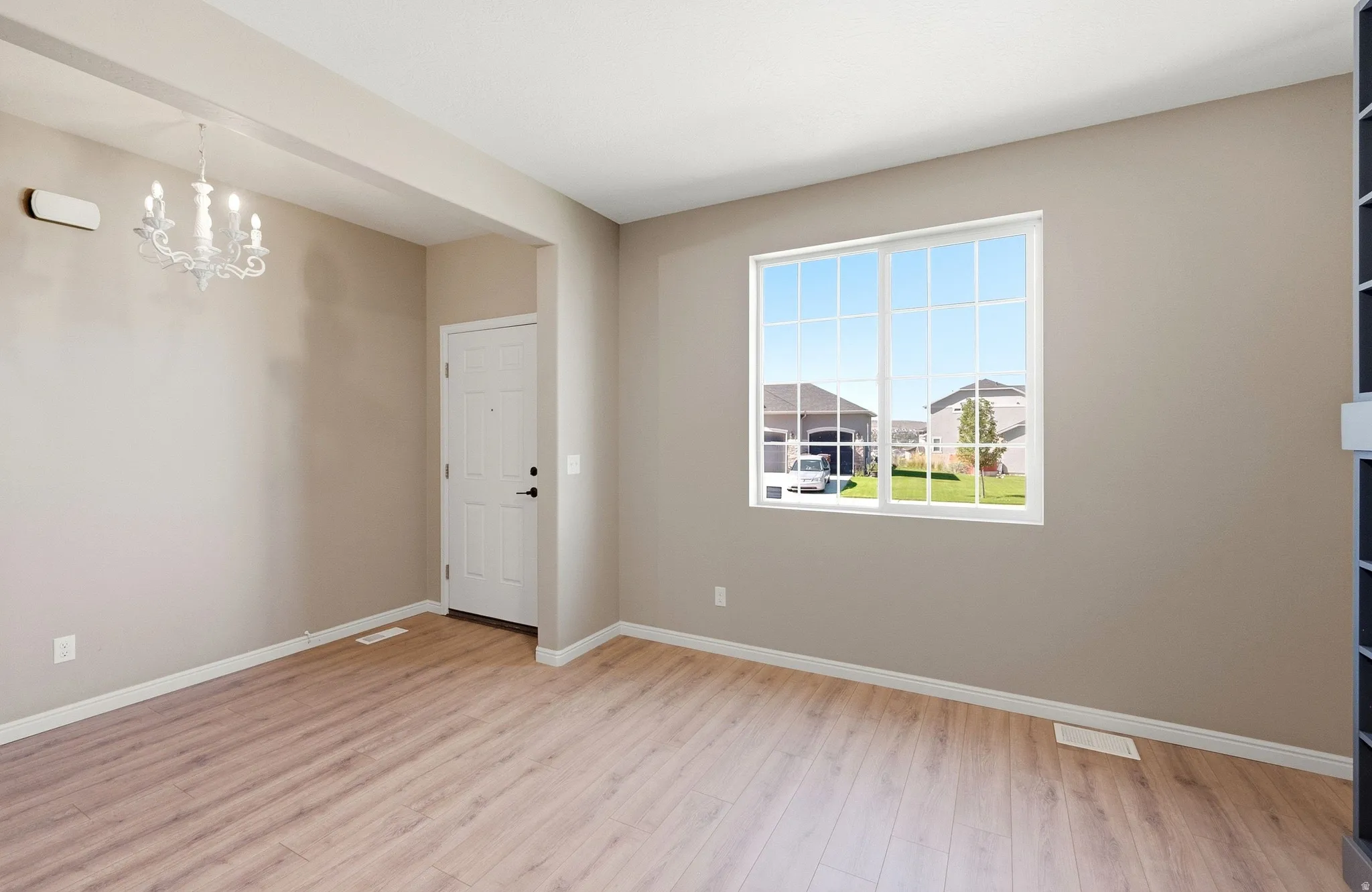 Wood-finish flooring, white window frames, front entry door, and a decorative chandelier