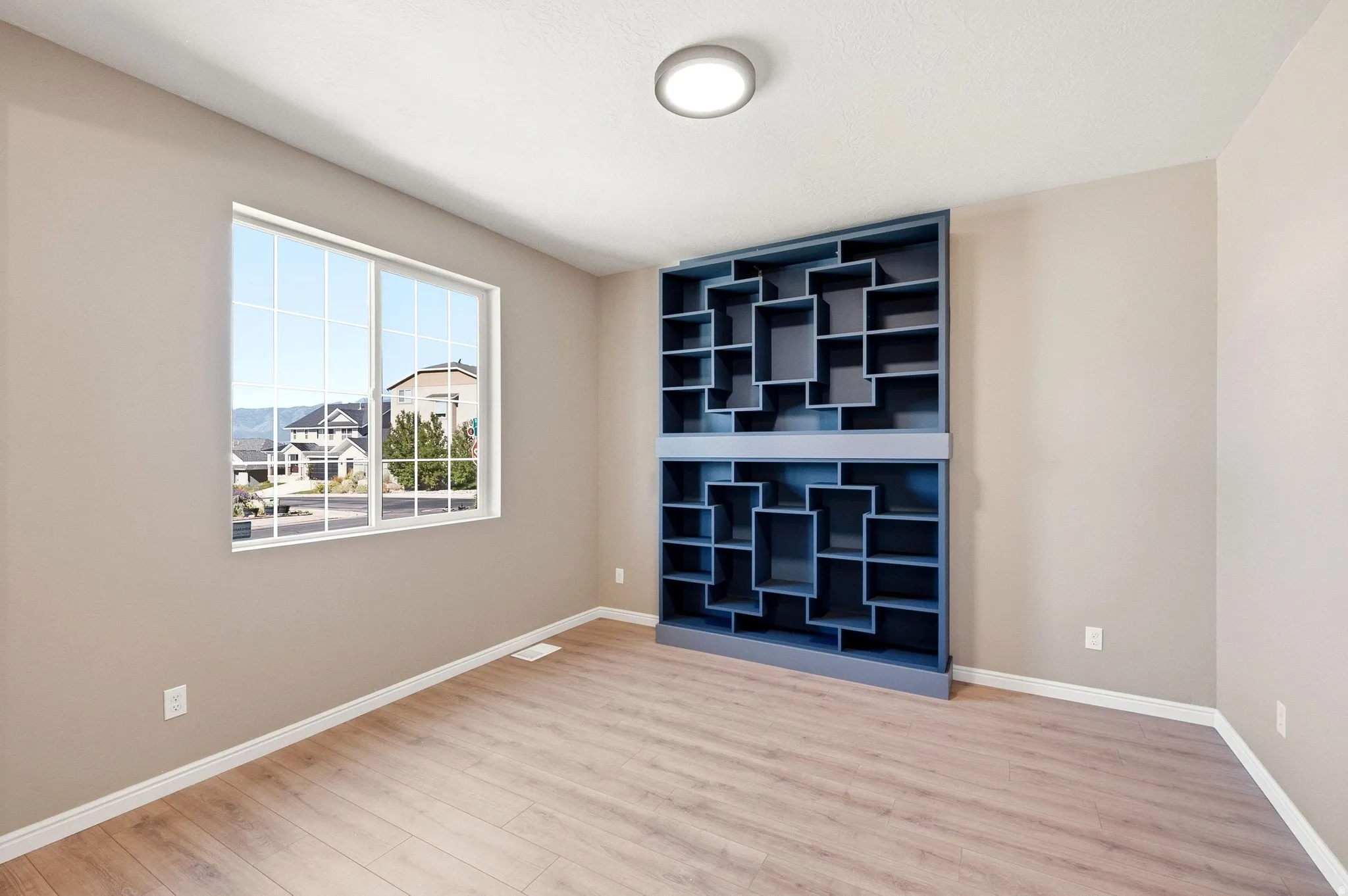 Built-in modular shelving unit, wood-finish flooring, white window trim, and overhead flush-mount lighting