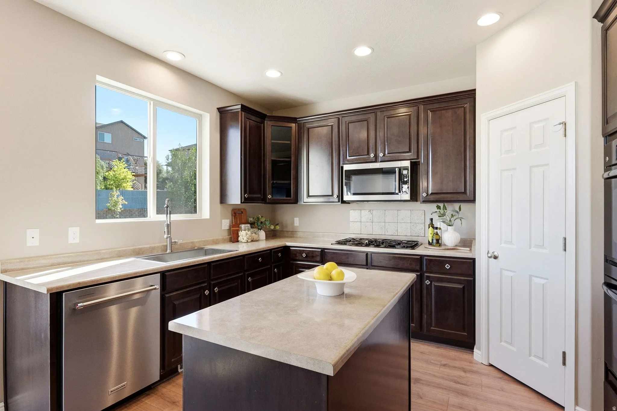 Kitchen featuring wood-finish flooring, dark wood cabinetry, light-toned countertops, and a large window