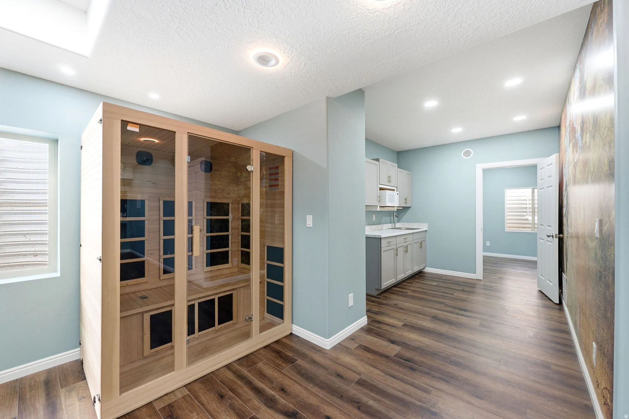 Wood-finish flooring, recessed lighting, light-toned cabinetry, built-in microwave, and a glass-enclosed sauna