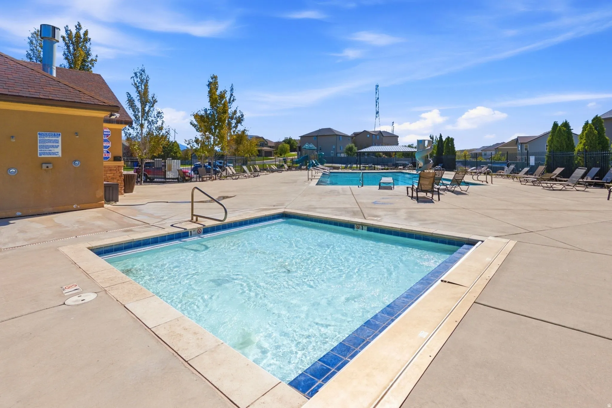 Concrete pool deck with integrated hot tub, adjacent to a large swimming pool with slide
