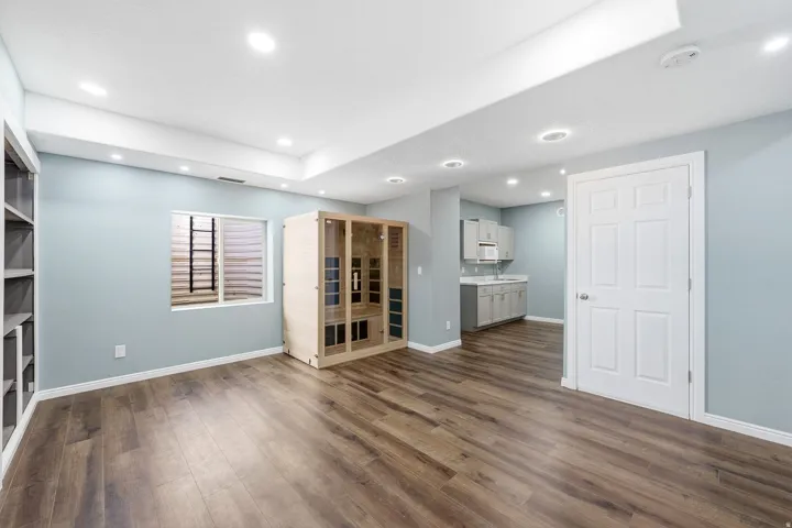 Recessed lighting, wood-finish flooring, built-in shelving, egress window, and a kitchenette with light gray cabinetry