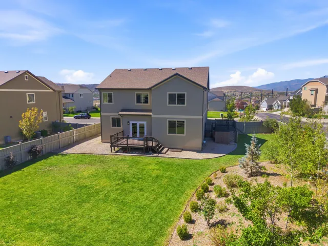 Expansive backyard featuring a manicured lawn, a built-in deck, and established landscaping