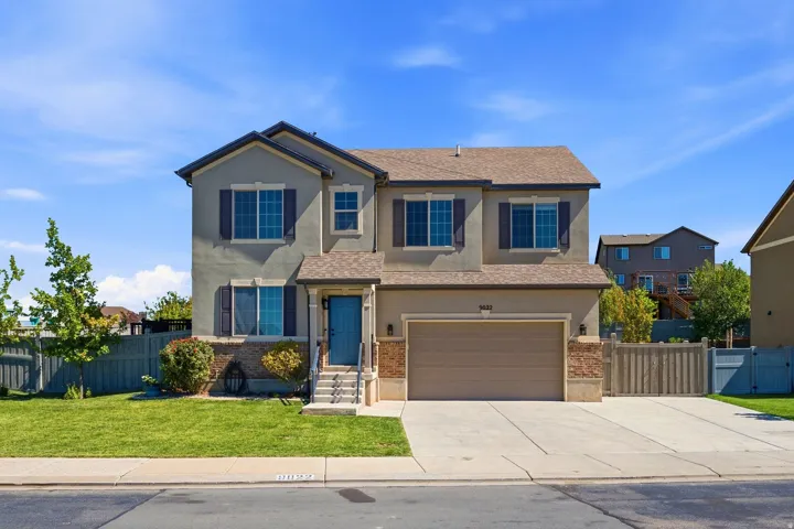 Two-story stucco exterior with stone accents, attached garage, concrete driveway, and a manicured lawn
