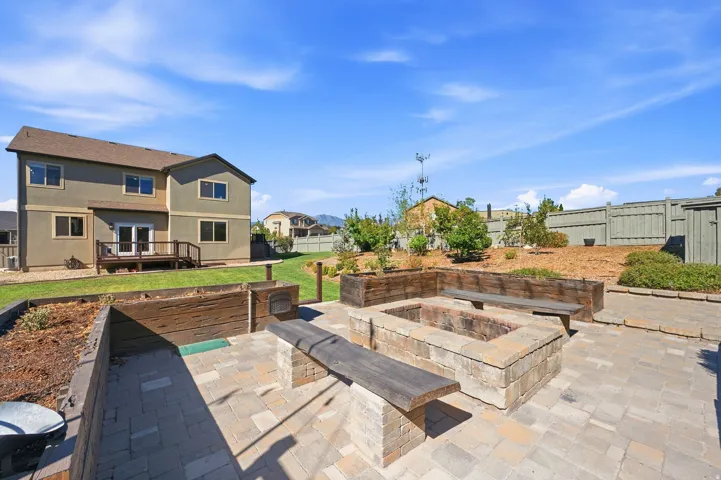 Paver patio with a built-in fire pit, integrated wood benches, and wood-sided raised garden beds