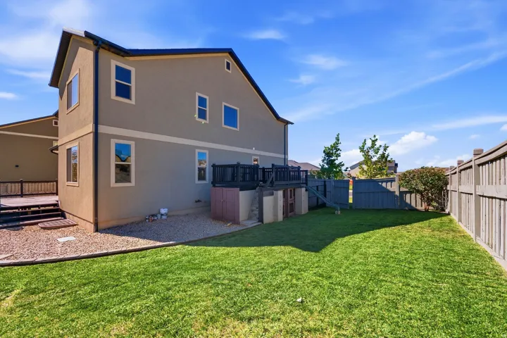 Expansive backyard featuring a manicured lawn, gravel landscaping, a privacy fence, and a multi-level deck