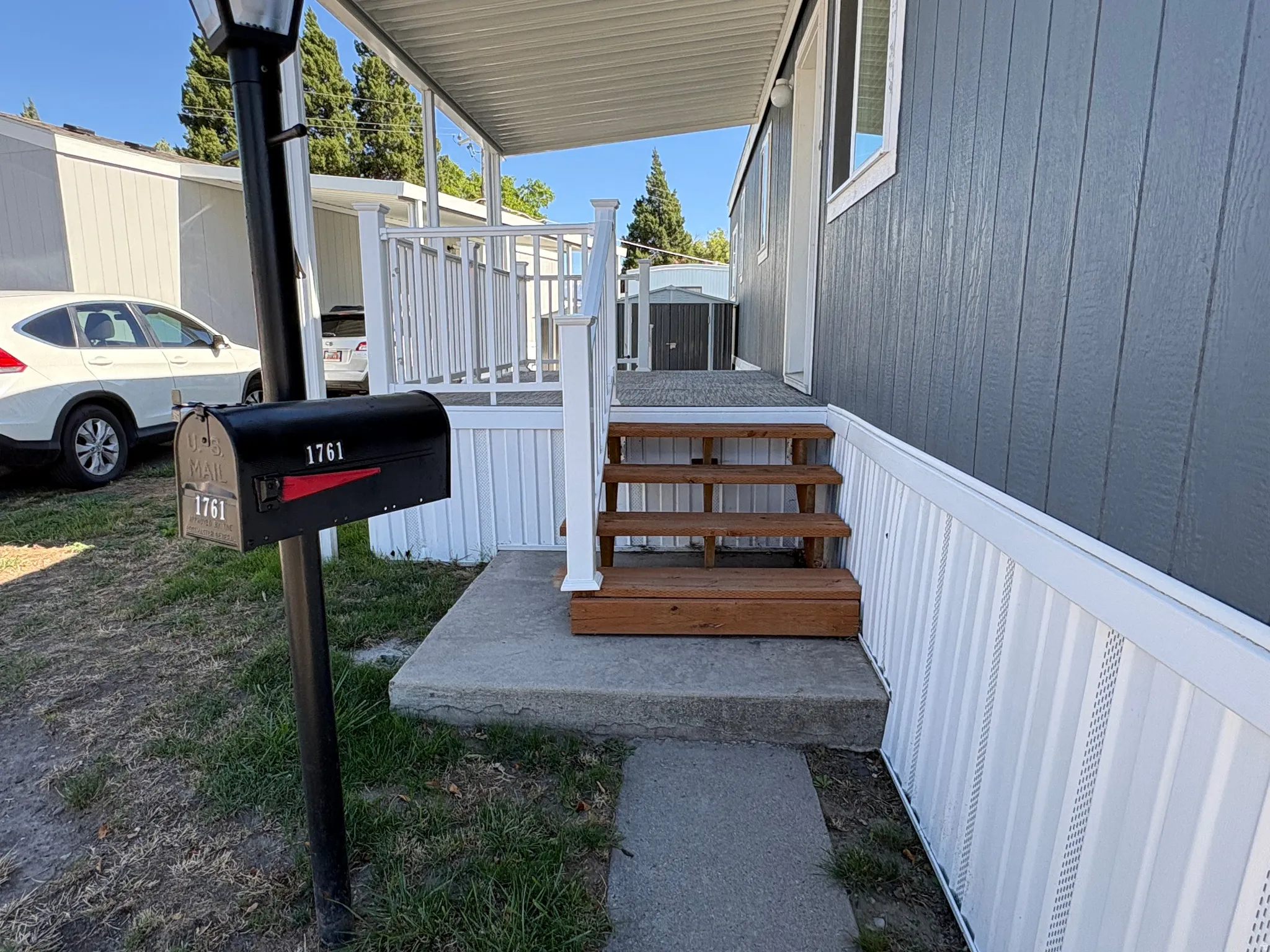 Siding with vertical paneling, white skirting, and a concrete pathway leading to a wooden staircase