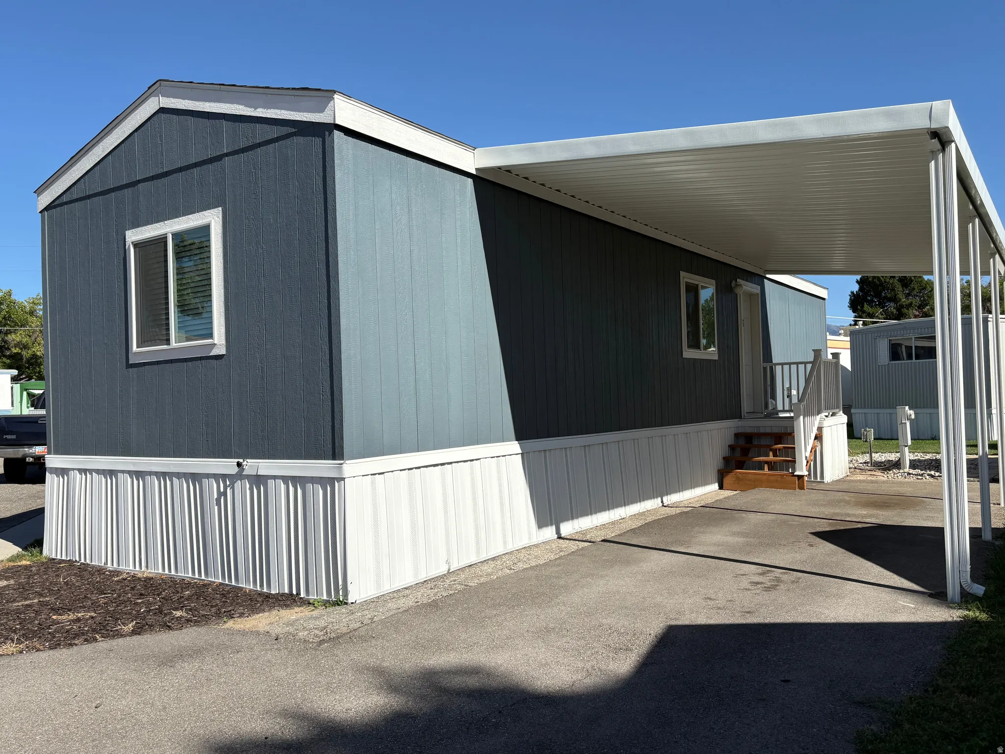 Exterior featuring vertical panel siding, a covered carport, wood-finish steps, and a white perimeter skirting