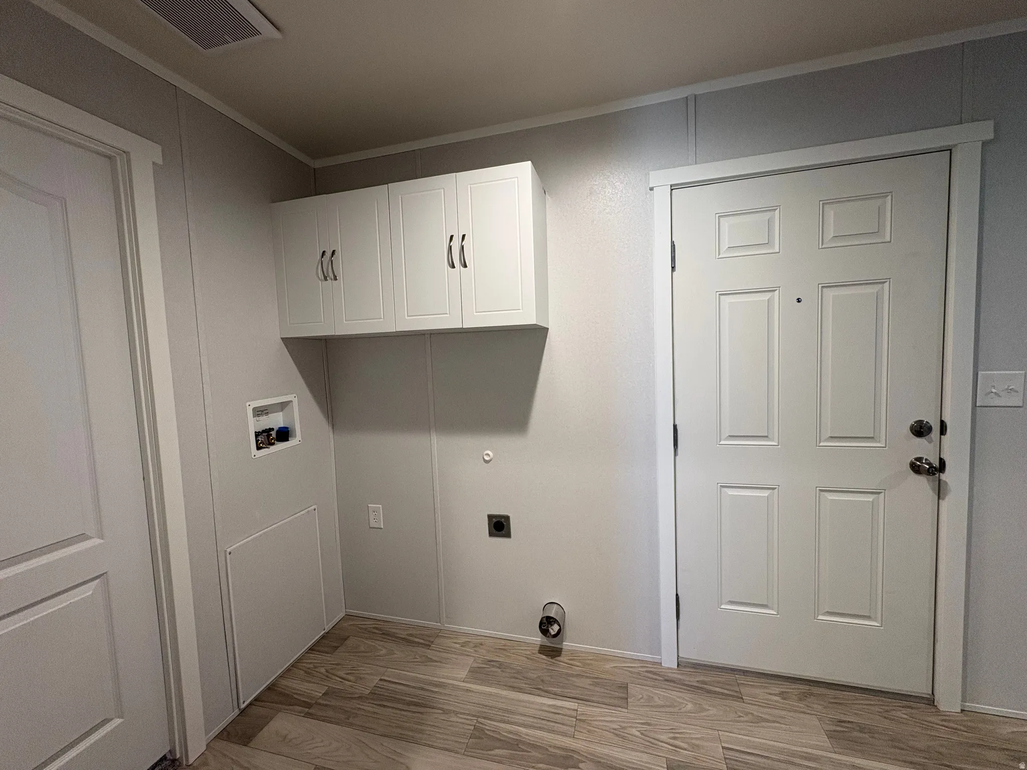 Laundry area with wood-finish flooring, overhead white cabinetry, and a panel door