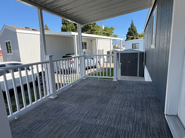 Covered porch with white railings, textured grey flooring, and an adjacent storage shed