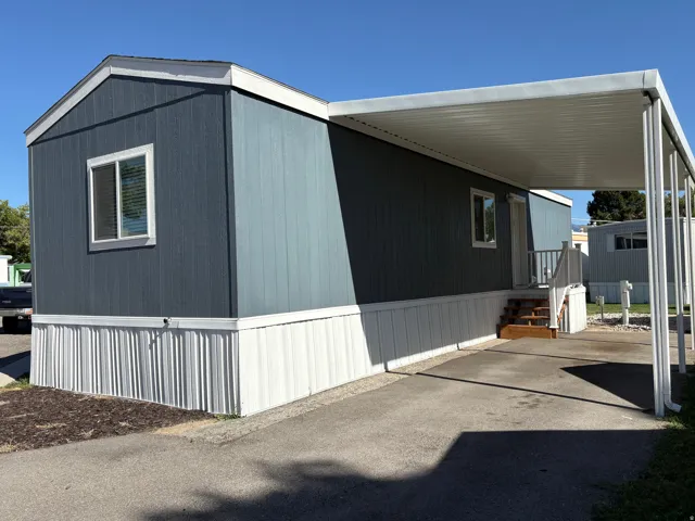 Exterior featuring vertical panel siding, a covered carport, wood-finish steps, and a white perimeter skirting