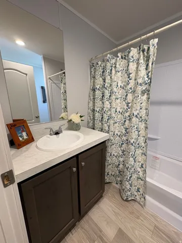 Full vanity with integrated sink, wood-finish flooring, and a full-size bathtub