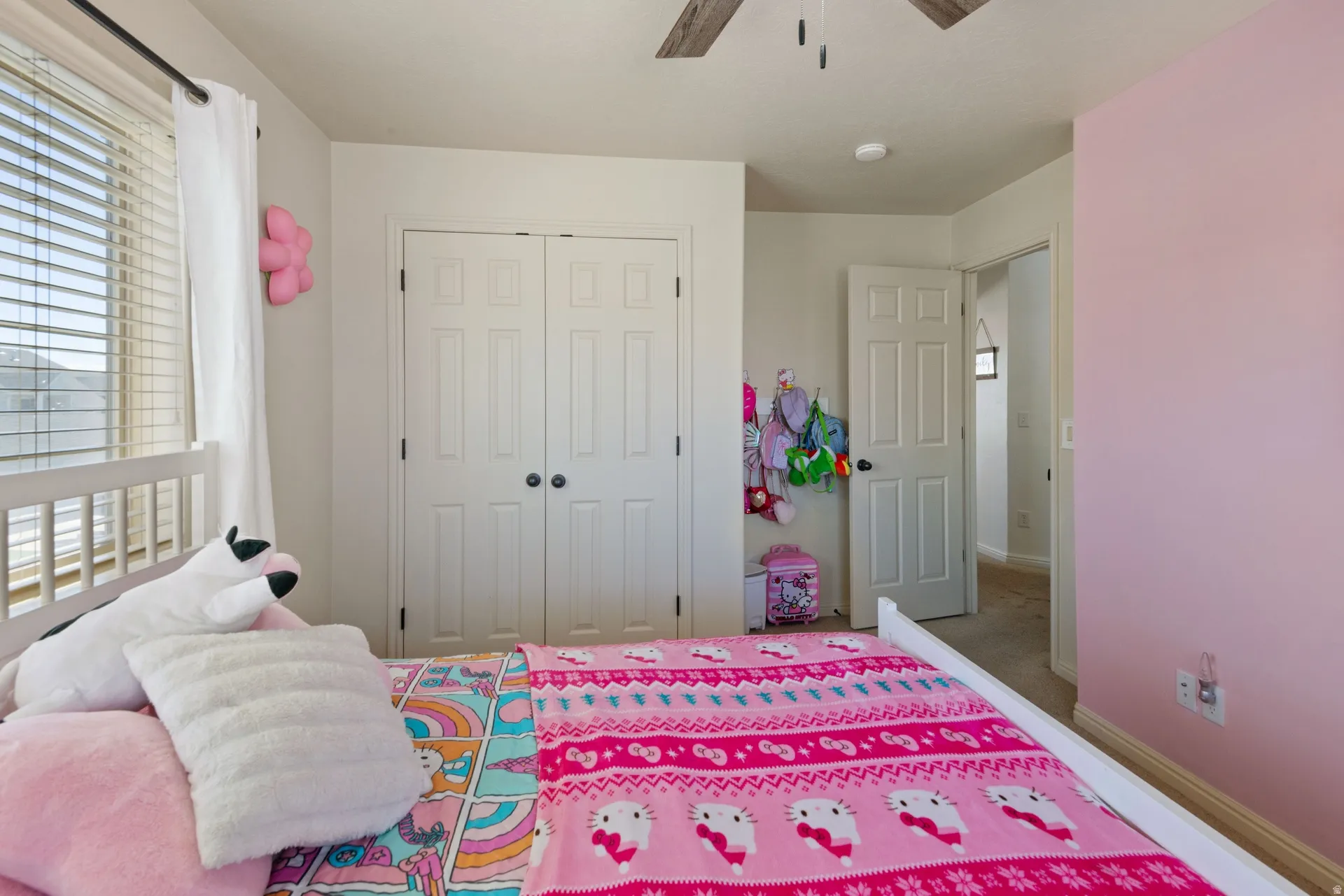 White paneled bi-fold closet doors with black hardware, window with horizontal blinds, and a ceiling fan