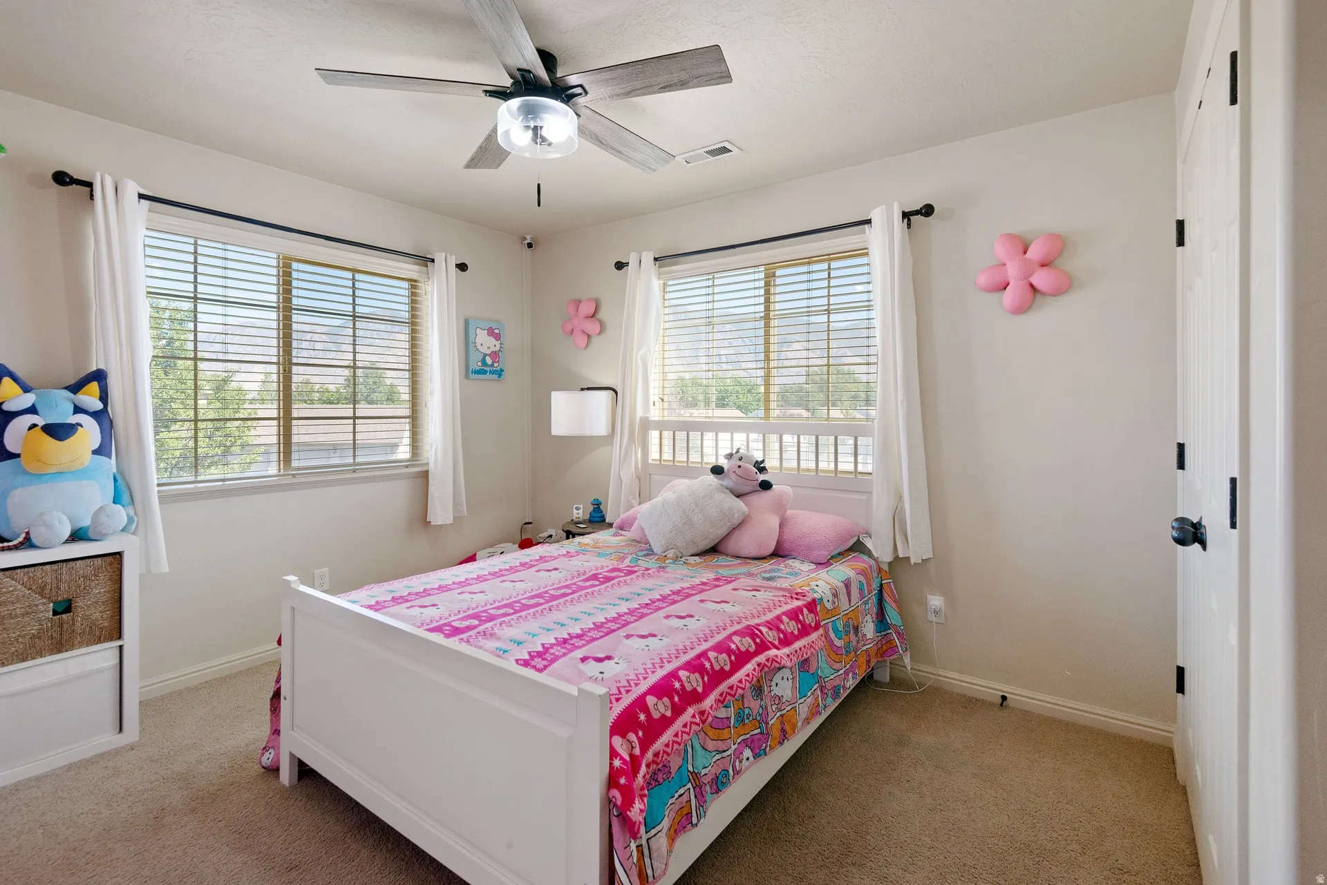 Carpeted flooring with a white paneled door, two windows with blinds, and a ceiling fan with integrated lighting