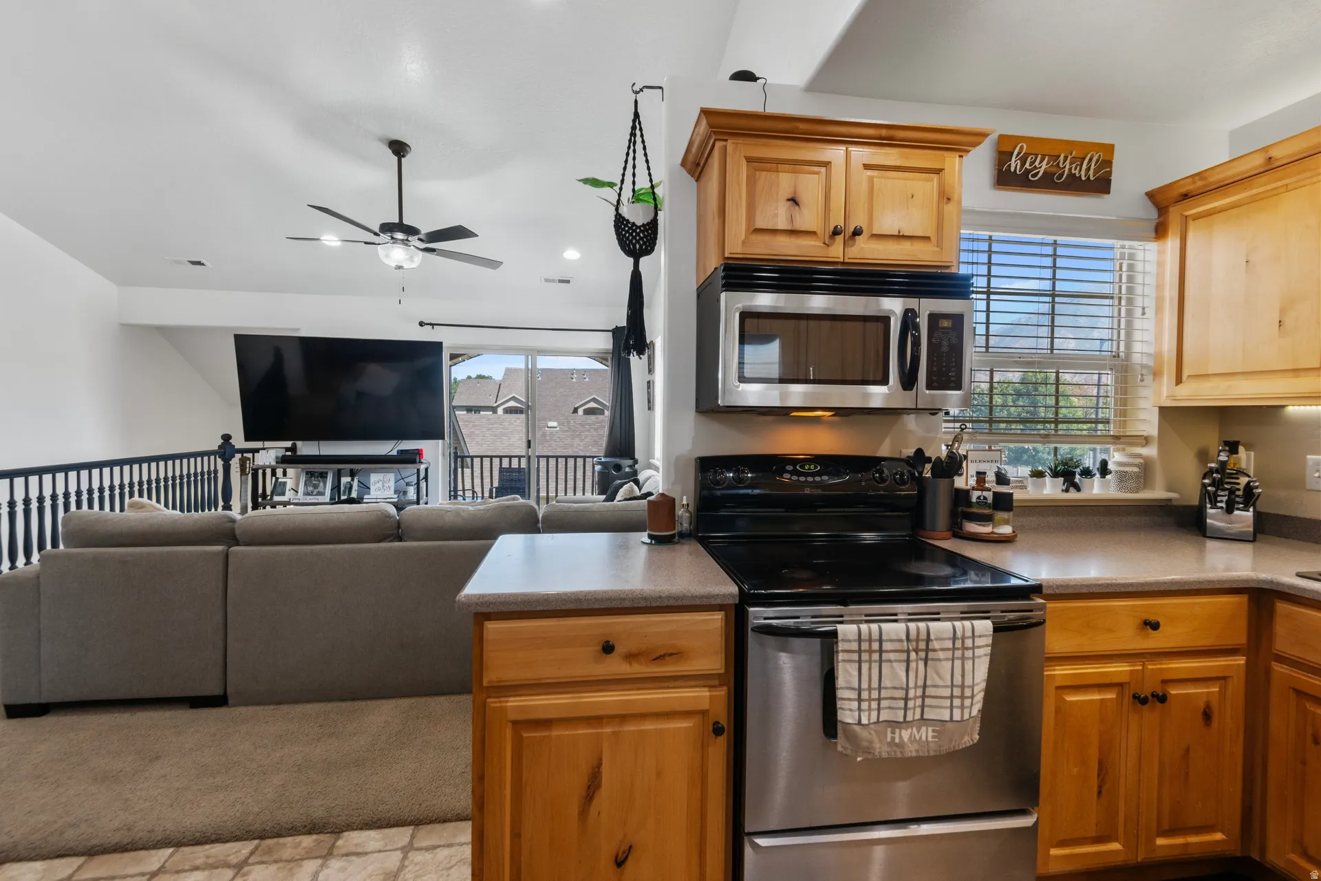 Kitchen featuring light wood cabinetry, stainless steel microwave, black electric range, and gray countertops