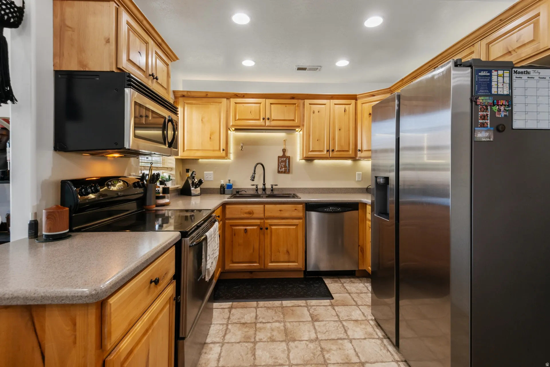Wood cabinetry with crown molding, stainless steel appliances, light-toned countertops, recessed lighting, and tile flooring