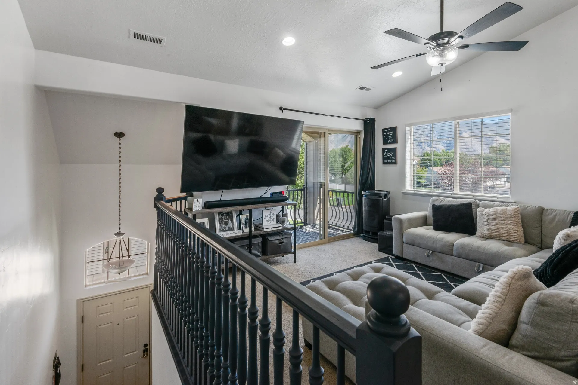 Vaulted ceilings, contemporary ceiling fan, sliding glass door with balcony, large window, and dark wood-finish railing