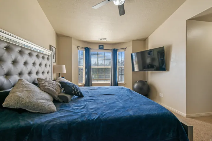 Bay window with blinds, ceiling fan, wall-mounted television, and neutral-toned carpeting
