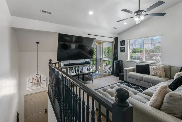 Vaulted ceilings, contemporary ceiling fan, sliding glass door with balcony, large window, and dark wood-finish railing