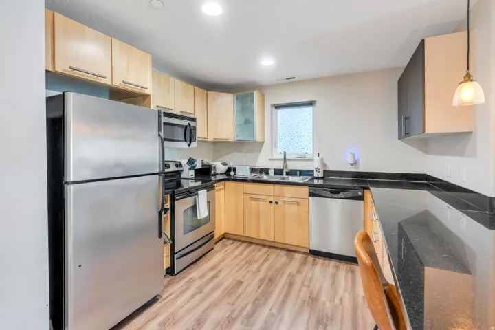 Kitchen featuring wood-finish flooring, stainless steel appliances, black countertops, light-toned cabinetry, and recessed lighting