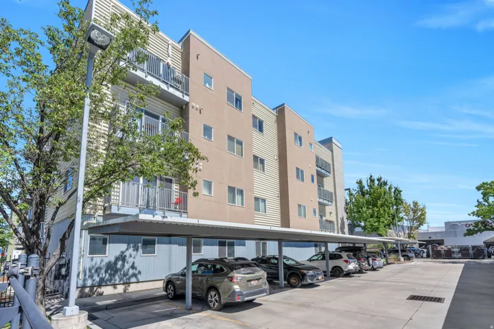 Multi-story building exterior with balconies, covered parking area, and a paved parking lot
