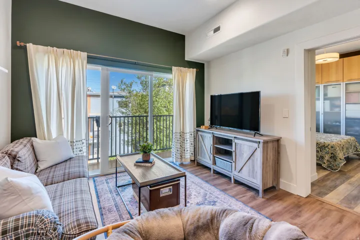 Sliding glass door leading to a balcony with black metal railing, wood-finish flooring, and high ceilings