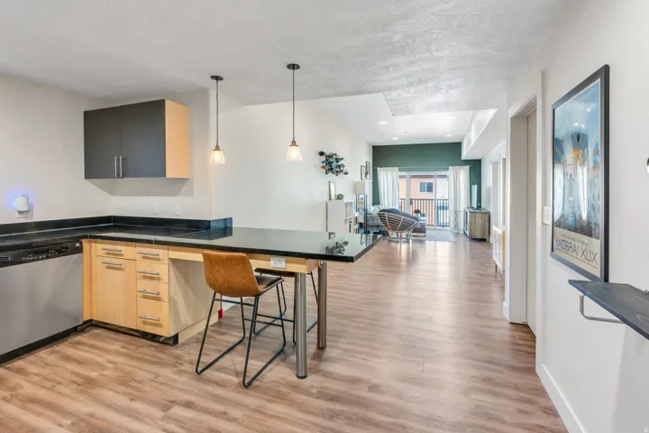 Wood-finish flooring throughout, stainless steel dishwasher, dark countertops, pendant lighting, and a private balcony