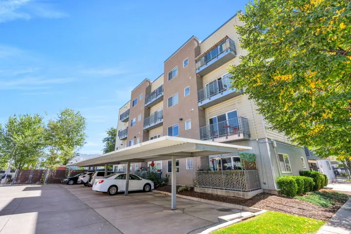 Multi-story apartment building with covered parking, private balconies, modern exterior finishes, and established landscaping