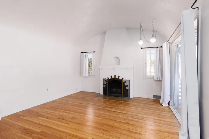 Hardwood flooring, arched ceiling, fireplace with decorative metal surround, white painted walls, and natural light from multiple windows