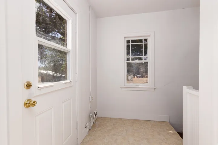 White paneled door with glass insert, single-hung window with grilles, white interior walls, and light-toned flooring