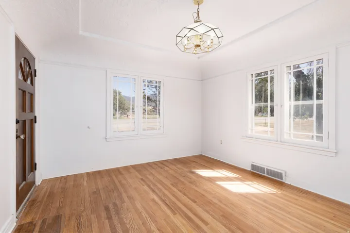 Hardwood flooring, decorative glass paneled entry door, two multi-pane windows, ceiling-mounted light fixture, and crown molding