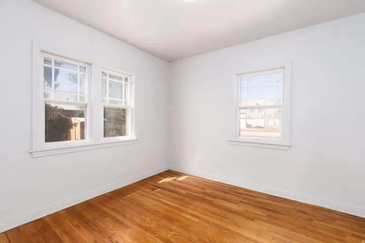Hardwood flooring, multiple windows with white trim, white walls, and a ceiling-mounted light fixture