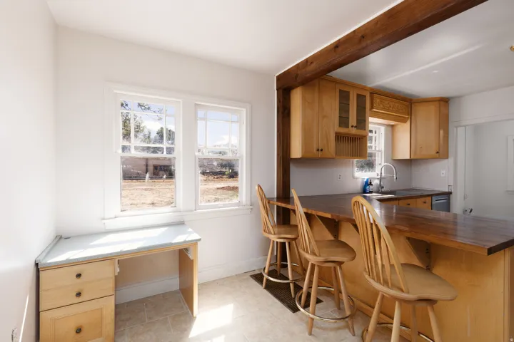 Light wood-finish cabinetry with glass accents, wood-finish countertops, stainless steel sink, tile flooring, and exposed wood beam