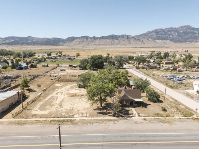 Mountain backdrop, mature trees, single-story residence, gravel road, fenced property