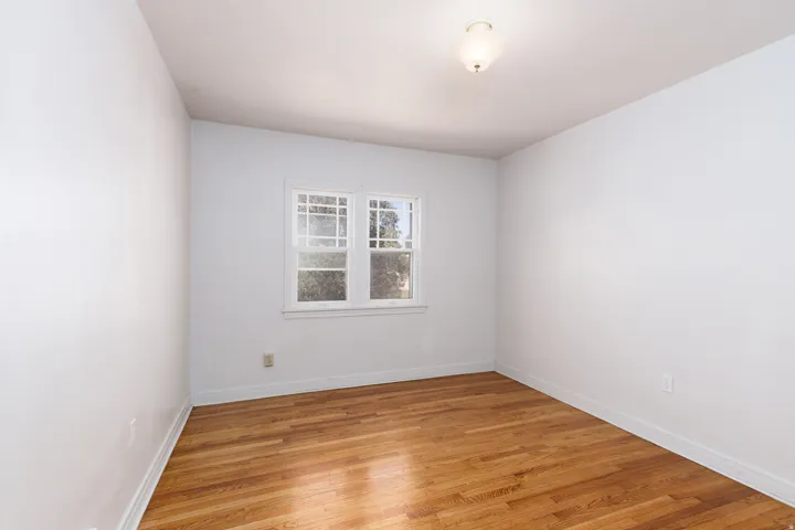 Wood-finish flooring with white walls, a multi-pane window, and a flush-mount ceiling light