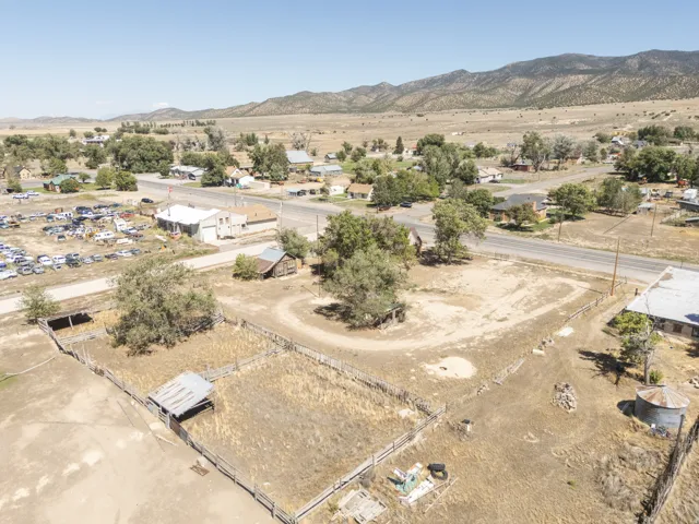 Expansive property with a rural setting, featuring a fenced enclosure, scattered mature trees, and a distant mountain backdrop