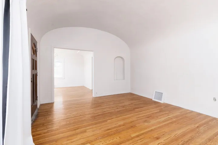 Arched ceiling details, built-in wall niche, original wood flooring, and a paneled entry door