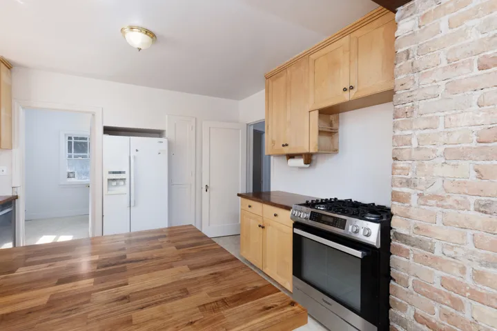 Kitchen featuring a butcher block island, light wood cabinetry, exposed brick detailing, and a stainless steel range