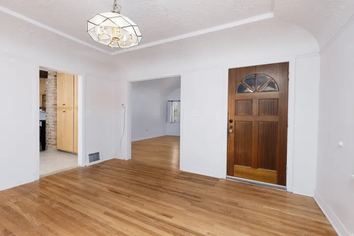 Hardwood flooring throughout, featuring a paneled entry door with an arched window, and a geometric semi-flush mount ceiling fixture