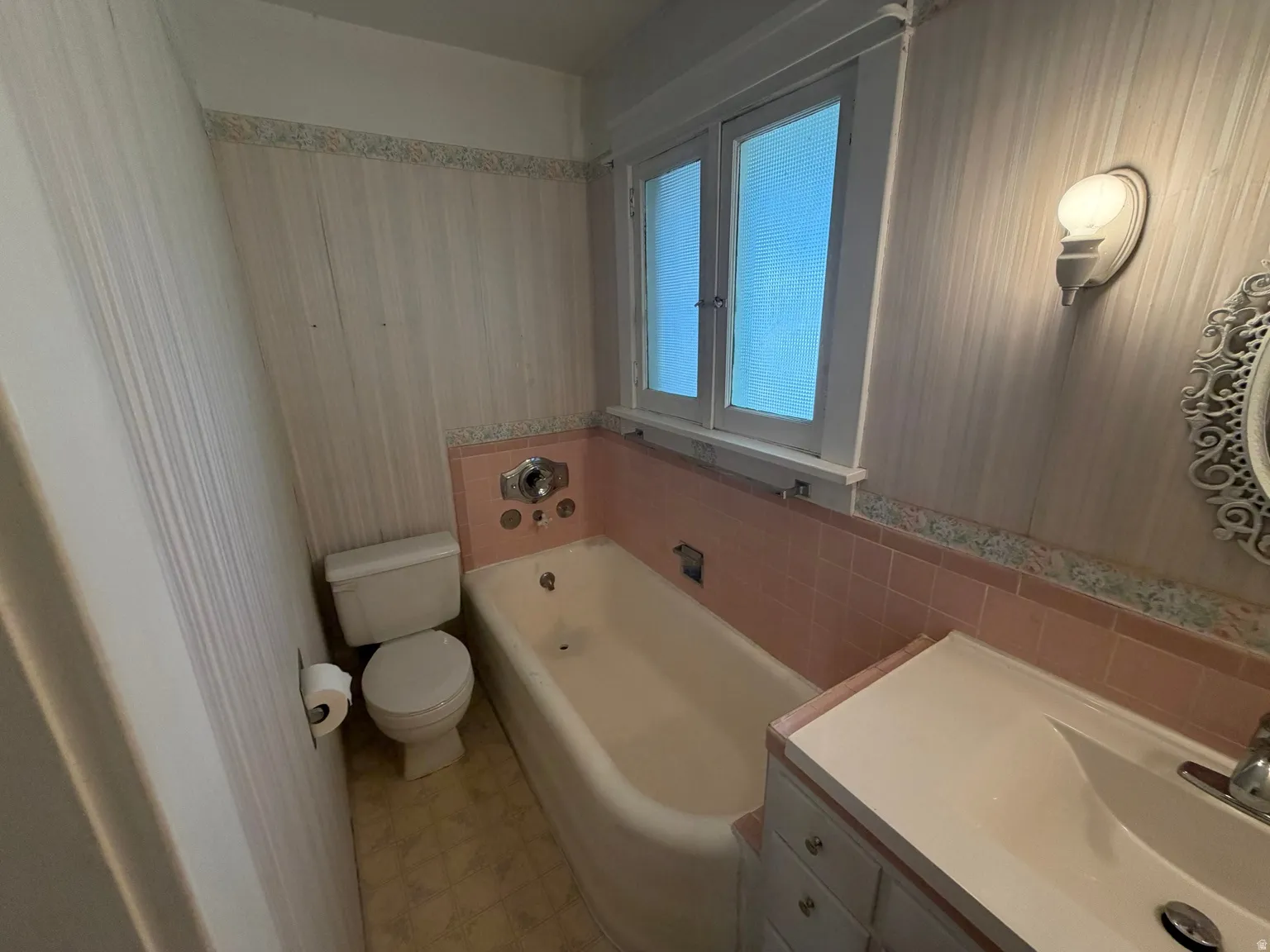 Bathroom featuring a built-in tub, tiled surround, dual windows, vanity with integrated sink, and an attached toilet