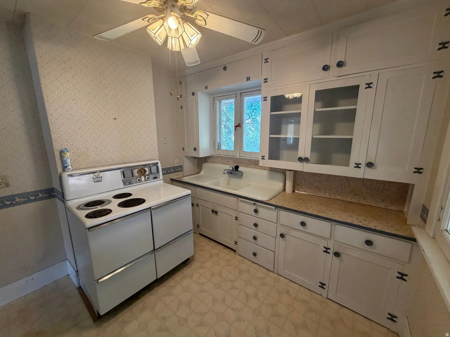 White painted cabinetry, built-in wall oven, white drop-in sink, patterned flooring, and a ceiling fan with integrated lighting