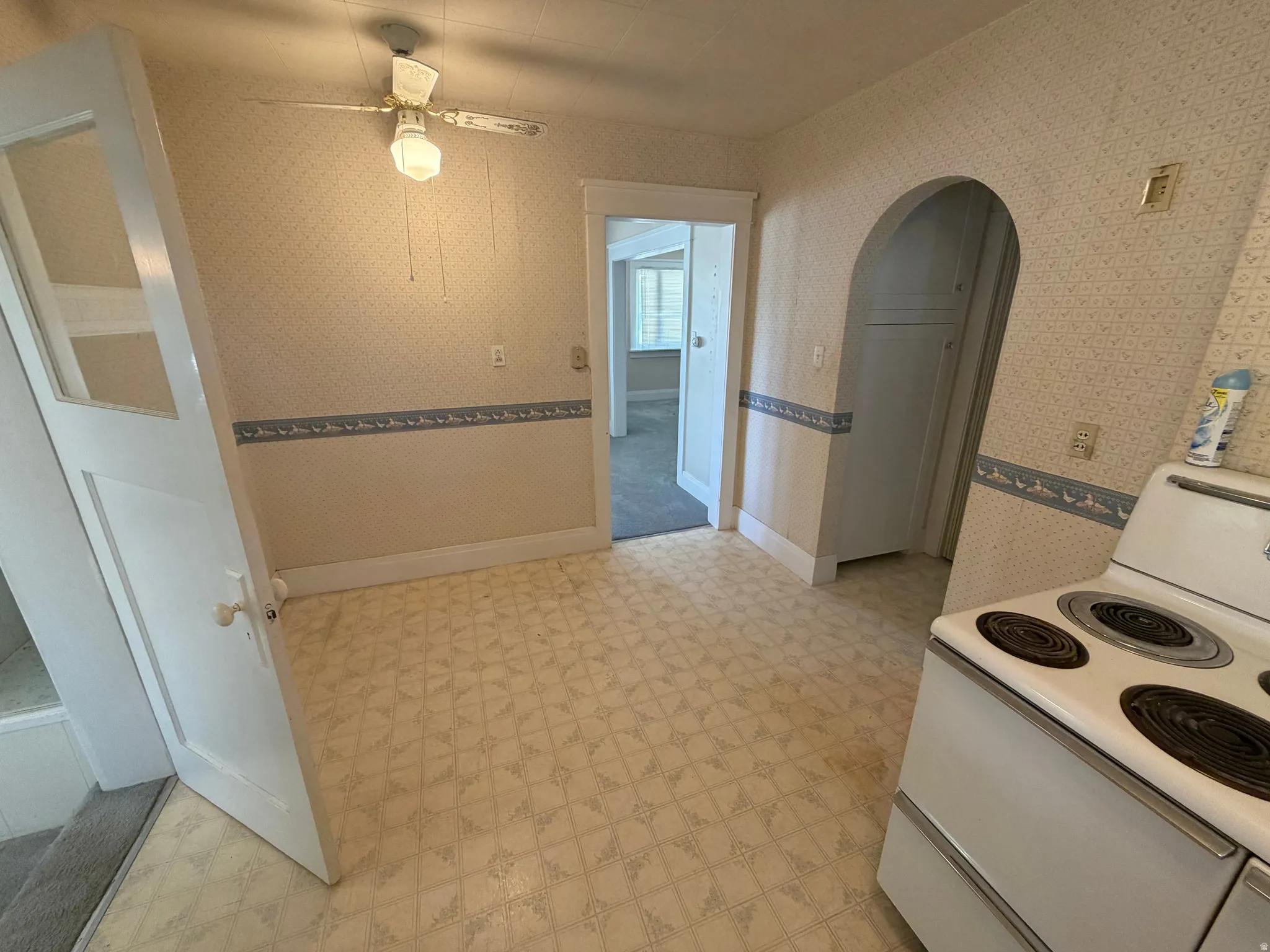 Patterned flooring, ceiling fan with light fixture, white range, arched doorway, and built-in cabinetry