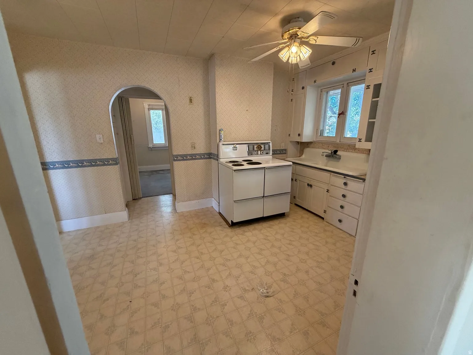 Kitchen area featuring vinyl flooring, an arched doorway, built-in cabinetry, a window with a sink, and a ceiling fan