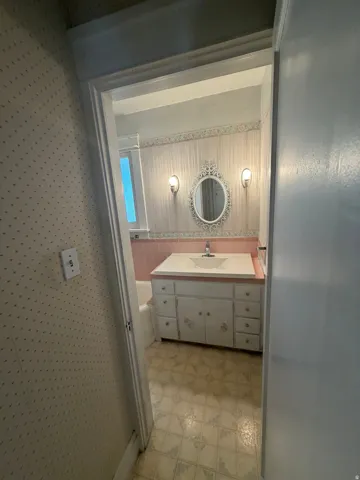 Bathroom featuring a built-in vanity with an integrated sink, wall-mounted sconces, and an ornamental mirror