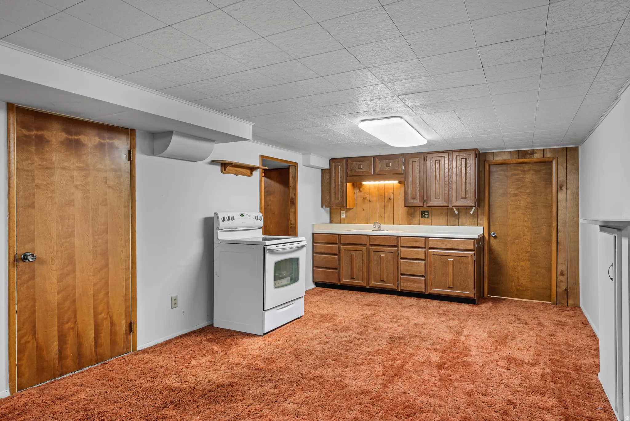 Kitchenette with wood-finish cabinetry, built-in sink, and range