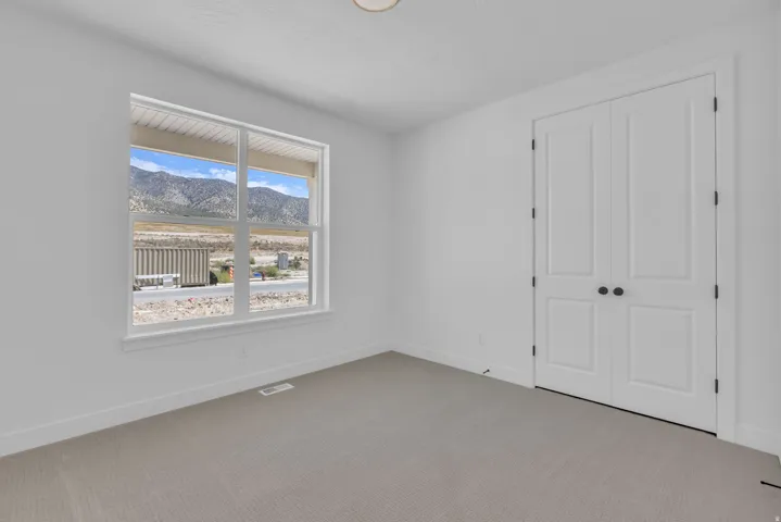 Large bedroom with mountain scenery through a large window, double panel closet doors and vaulted ceiling.