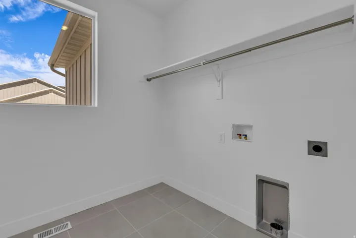 Oversized laundry room featuring a window, tile flooring, wall-mounted shelving, and plumbing hookups.