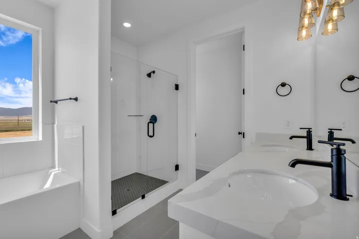Primary bath with dual undermount sinks with matte black fixtures, a Euro glass-enclosed large shower with tile flooring and surround, a built-in soaker tub with subway tile surround, and a large picture window with views to the open space to the side of