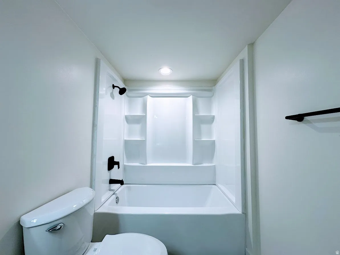 White bathtub with integrated shelving, matte black fixtures, and a ceiling-mounted light fixture